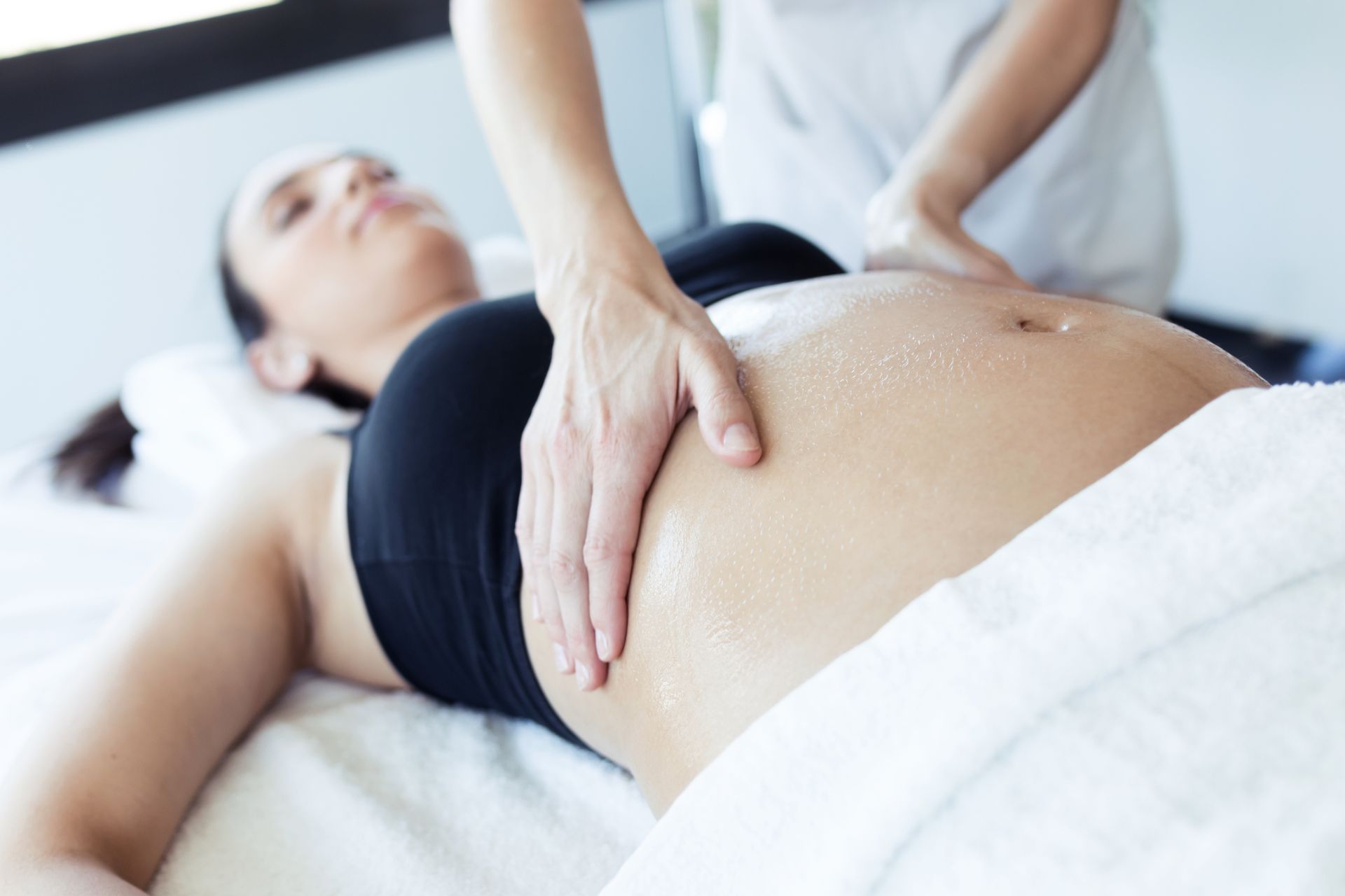 A pregnant woman is laying on a bed getting a massage.