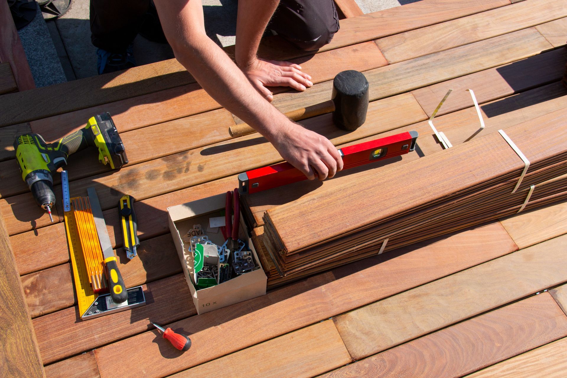 A person is measuring a piece of wood on a wooden deck.