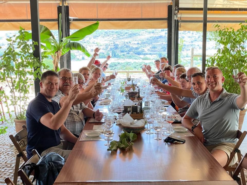 A group of people are sitting at a long table toasting with wine glasses.