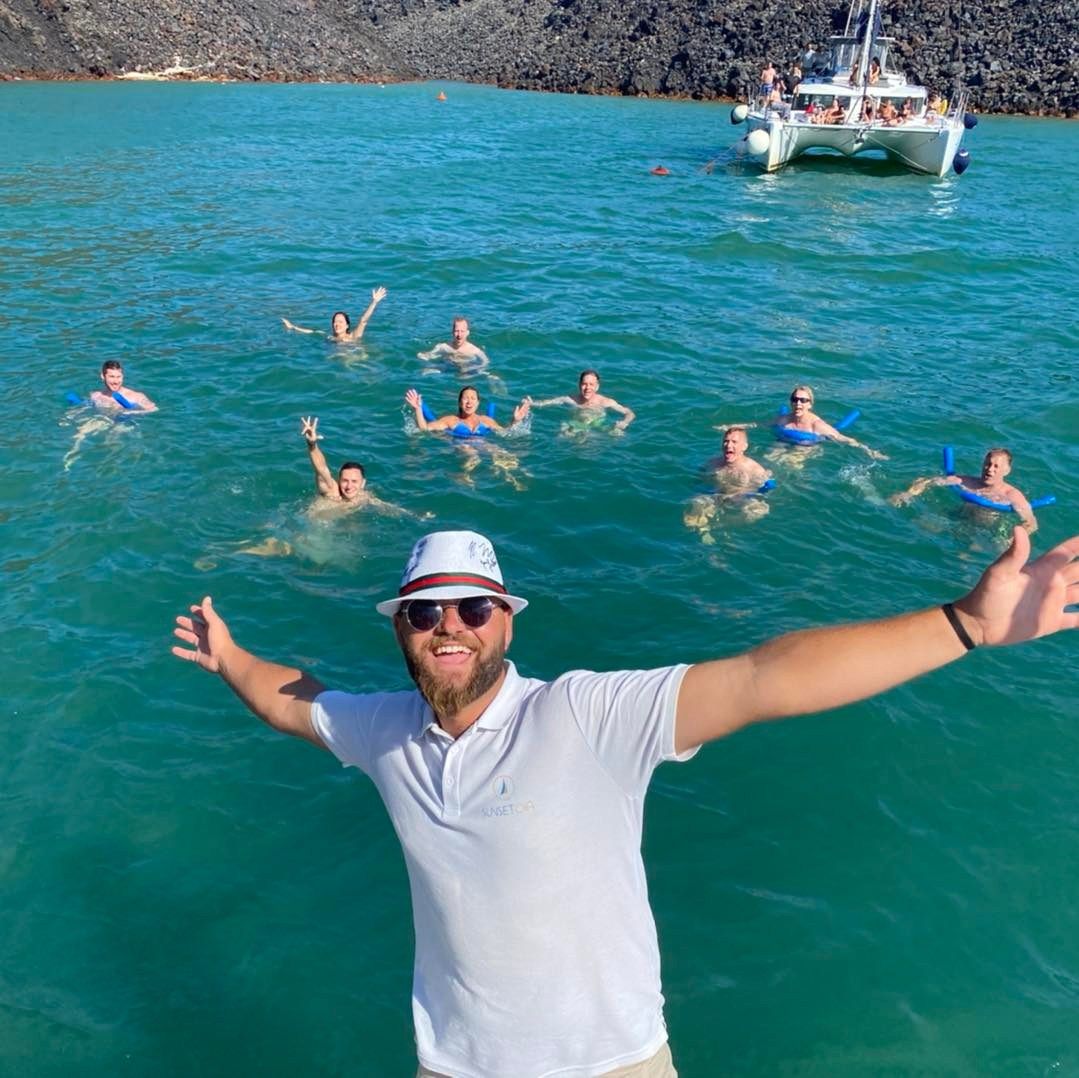 A man is standing in the water with his arms outstretched while people swim behind him.