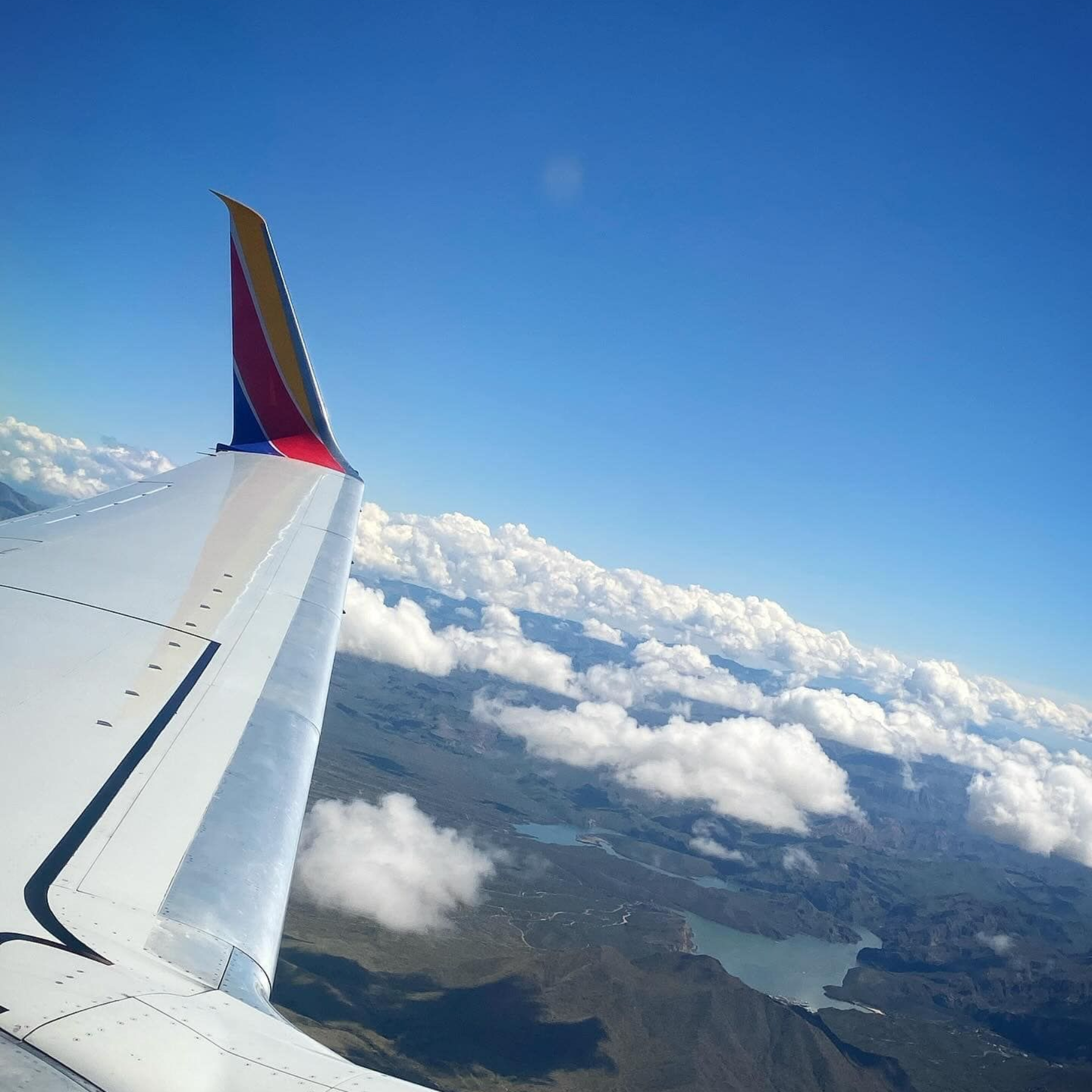 People waving from a hot air balloon basket; on a field, others watch. Red and white balloon above.