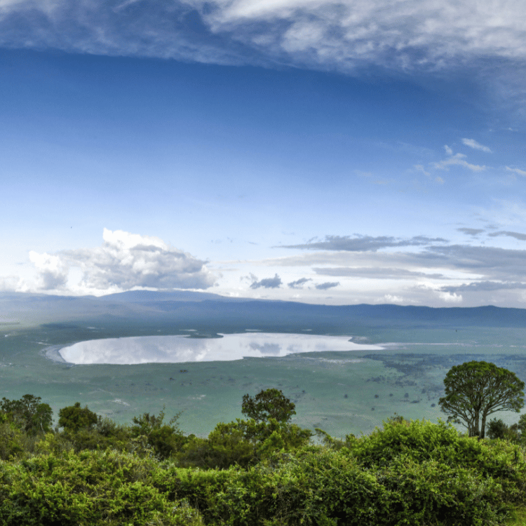 Scenic view of Ngorongoro Crater, Tanzania; lush green landscape, lake, and blue sky with clouds.