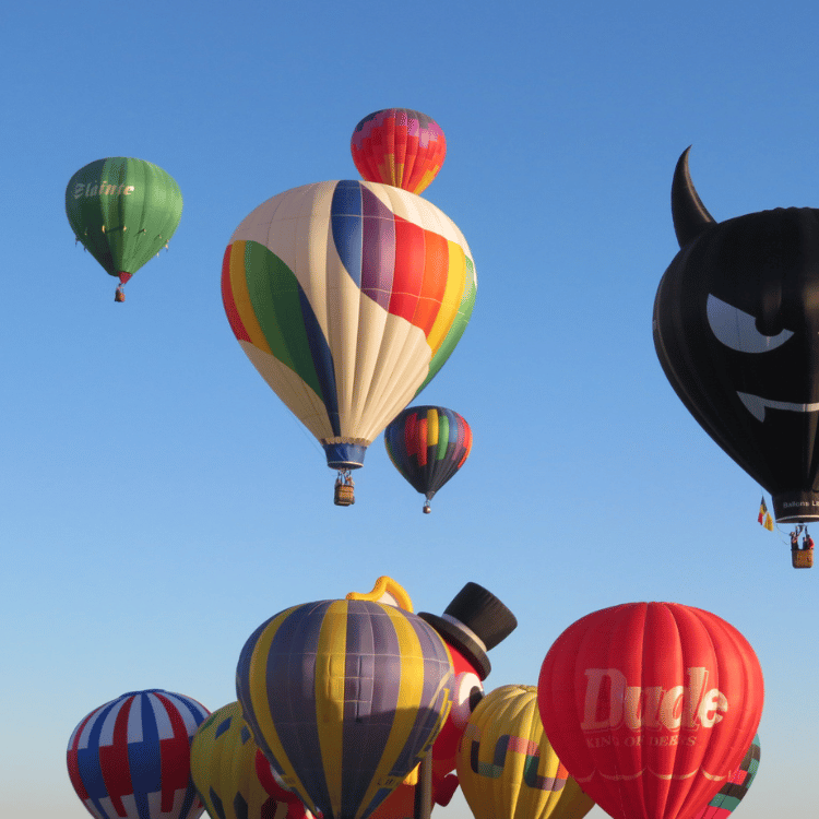 Hot air balloons of various colors and designs float in a clear blue sky.