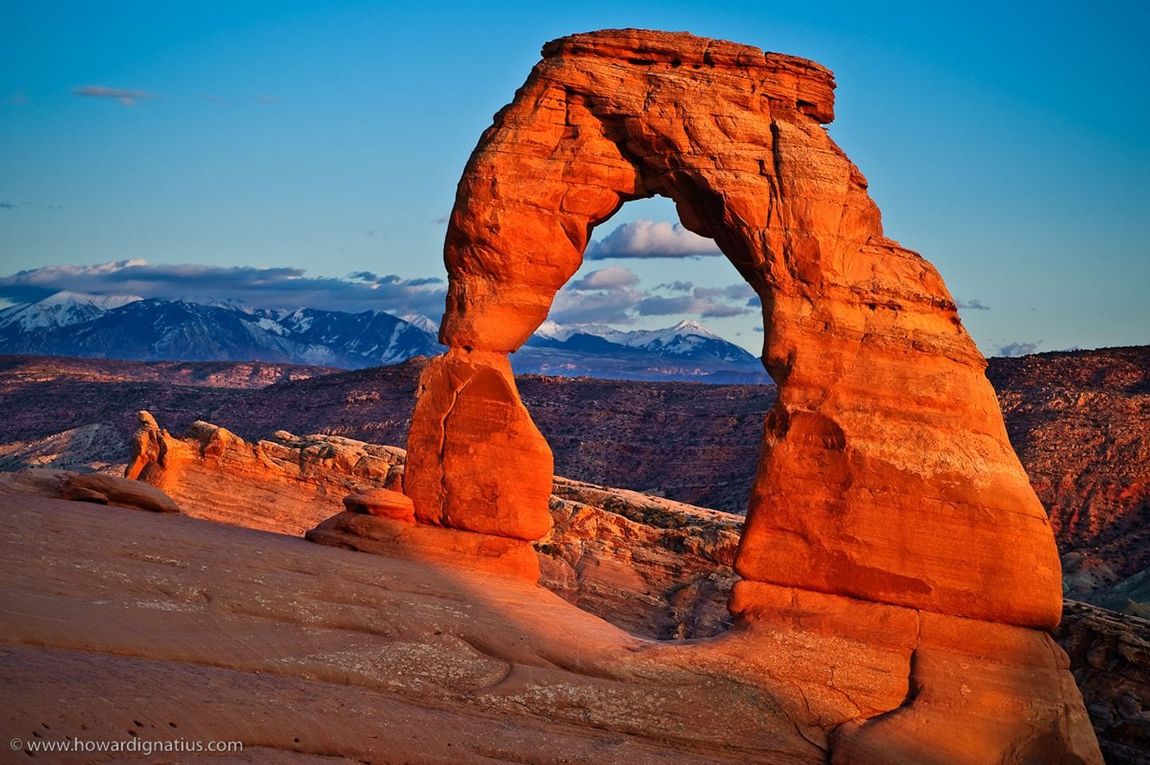 A large rock formation in the middle of a desert with mountains in the background.