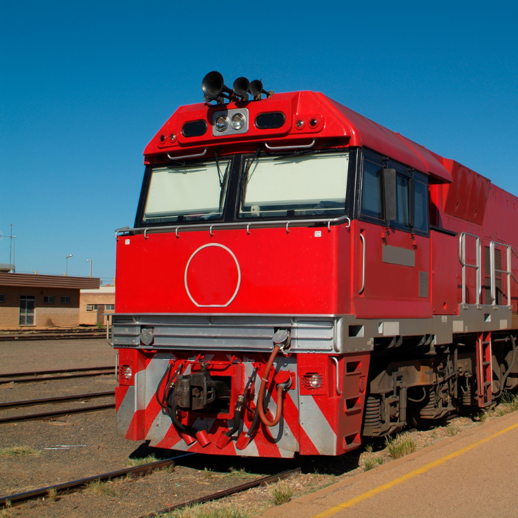 Red train engine on railway tracks under a clear blue sky.