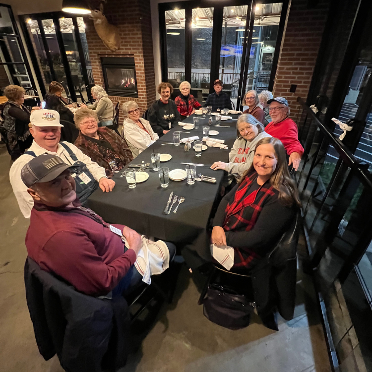 A group of people sit at a long table, dining in a restaurant.