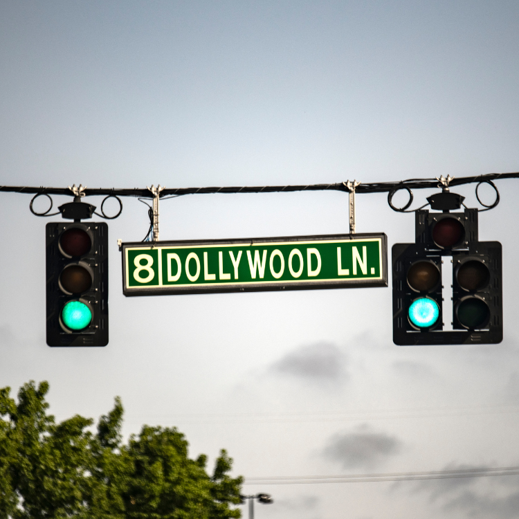 Green traffic lights and a "8 Dollywood Ln." street sign. Cloudy sky background.