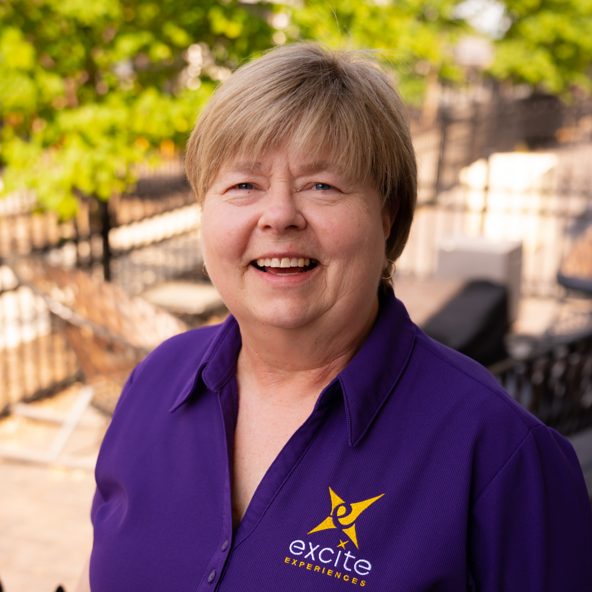 Woman with short blonde hair in purple shirt, smiling, with