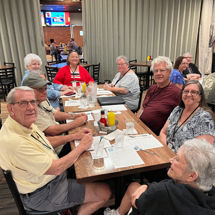 Group of seniors seated around a restaurant table, smiling, and looking at the camera.