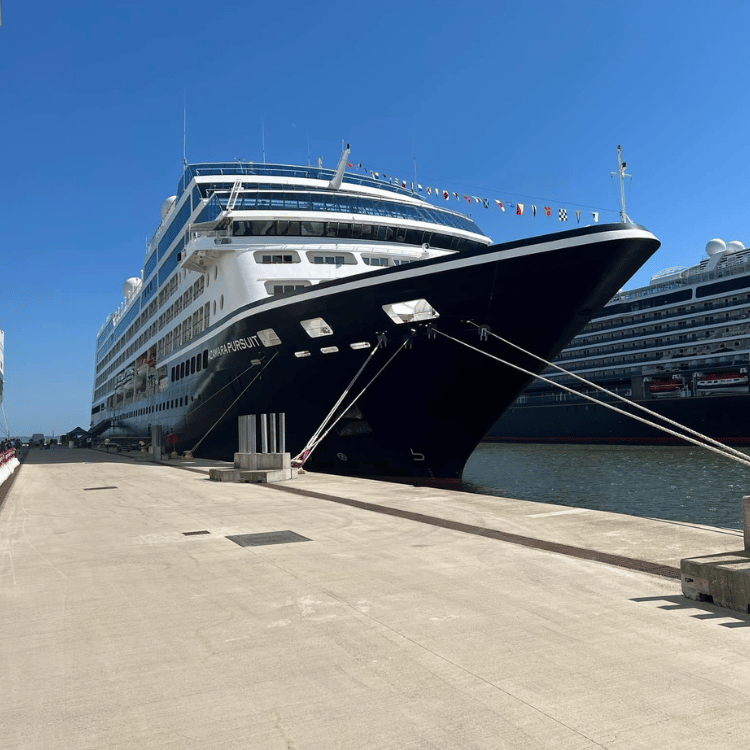 Large cruise ship docked at a pier, black hull, blue sky.
