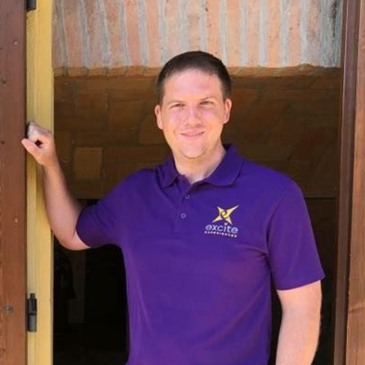 Man in purple polo shirt standing in a doorway; smiling, holding the doorframe.