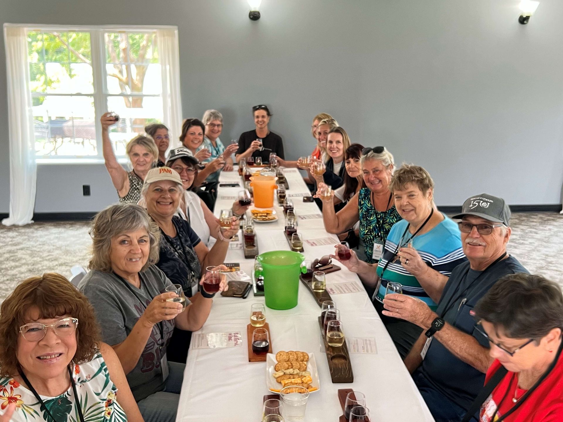 A group of people are sitting at a long table drinking wine.