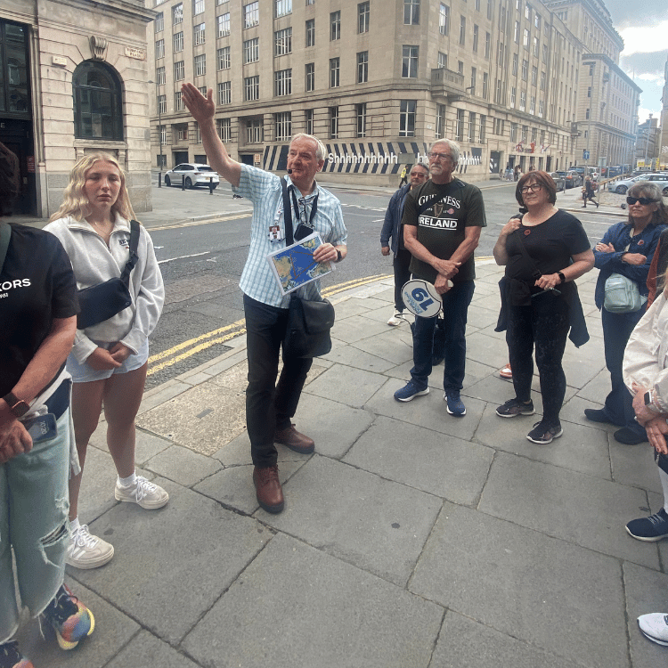 A tour guide gestures towards a building, leading a group of people on a city street.