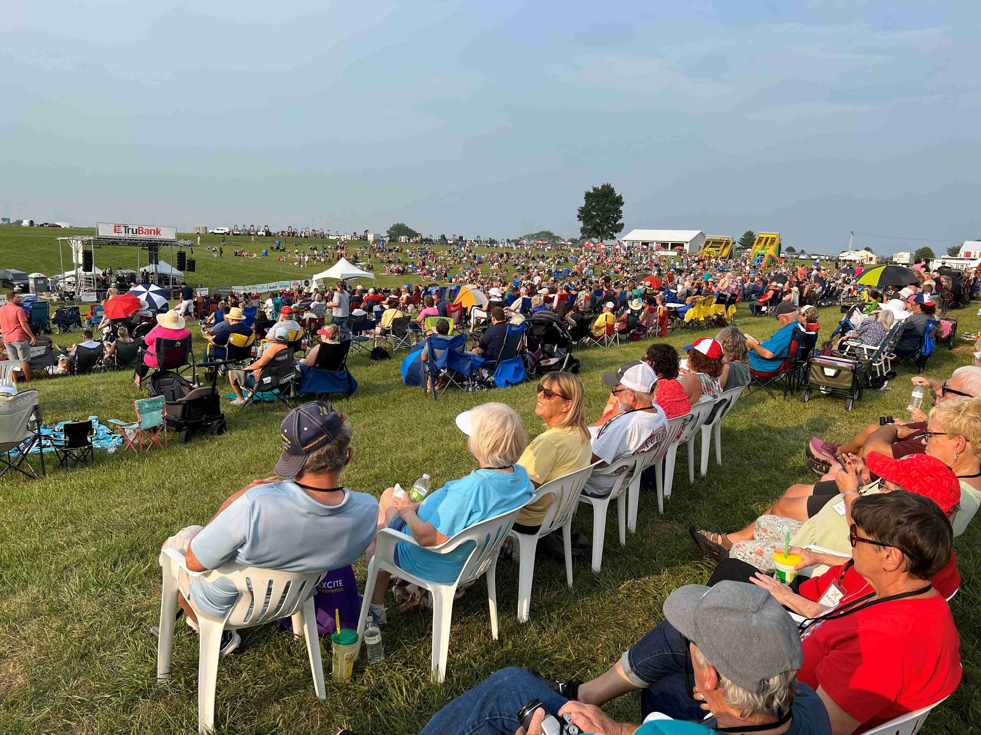 A large group of people are sitting in chairs in a field.
