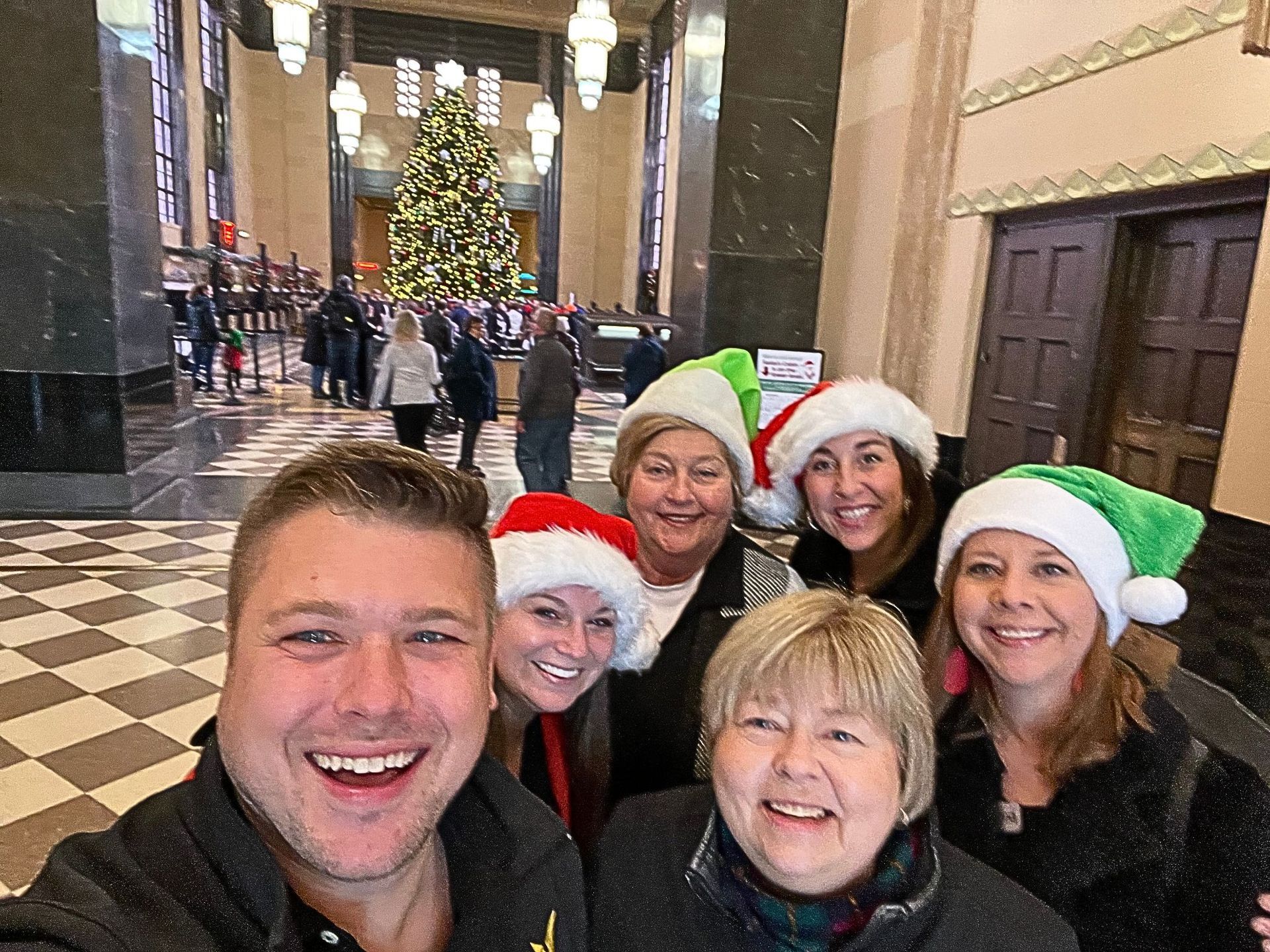 A group of people wearing santa hats are posing for a picture in front of a christmas tree.