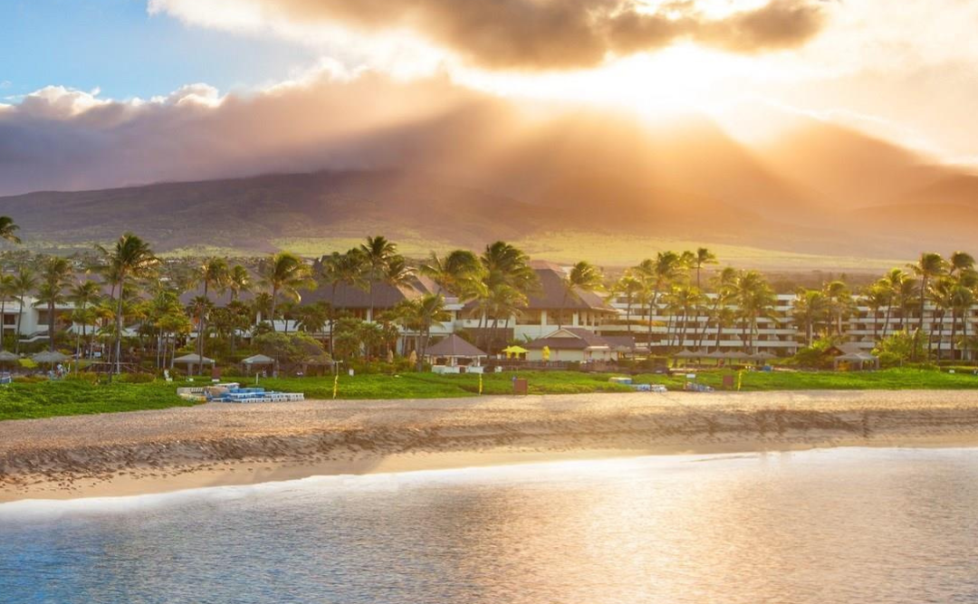 The sun is shining through the clouds over a tropical beach in Hawaii.