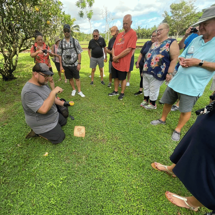 Group watches a man kneel and play a lawn game with a small wooden block and ball in a grassy area.