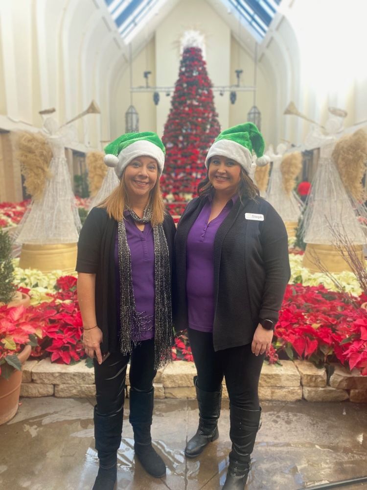 Two women wearing santa hats are standing next to each other in front of a christmas tree.