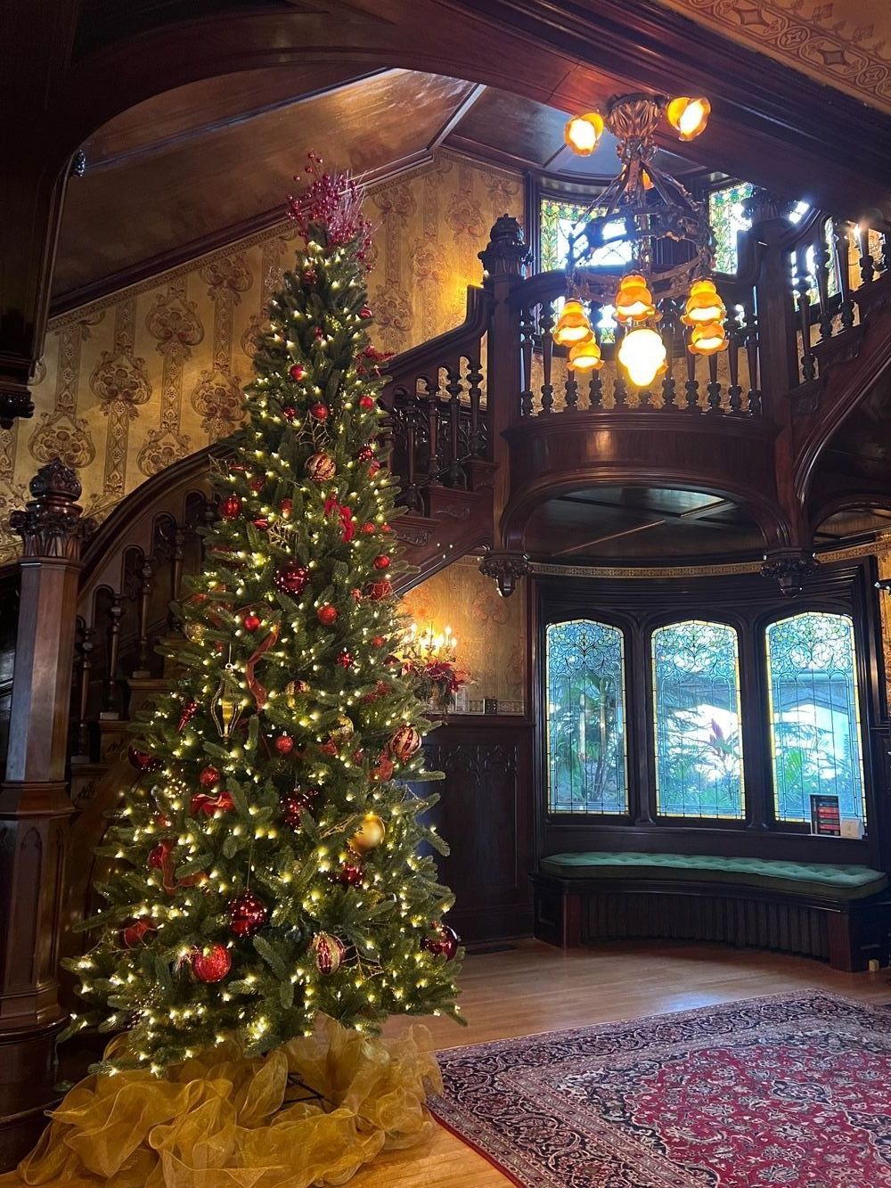 A christmas tree is sitting in the middle of a room next to a staircase.