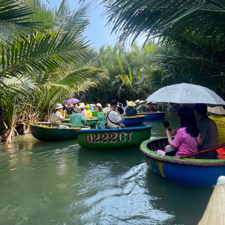Boats on a river surrounded by palm trees. People in boats, some with umbrellas, enjoy the sunny day.