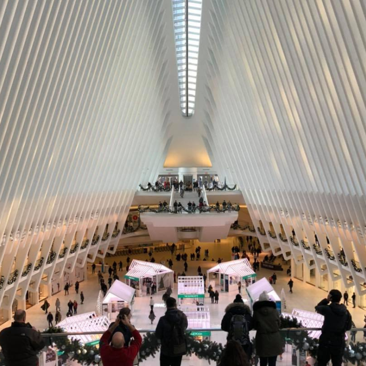 Inside the Oculus, NYC: White vaulted ceiling, shoppers below, people on balconies.