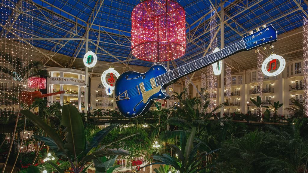 A large blue electric guitar is hanging from the ceiling of a building.