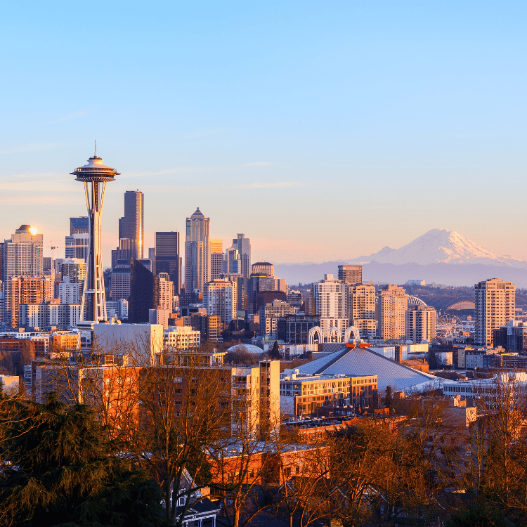 Seattle skyline with the Space Needle, buildings, and Mt. Rainier under a blue sky at sunset.