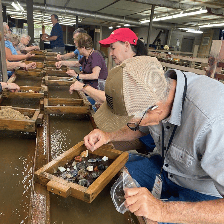 People panning for gems in a water trough, under a covered area.
