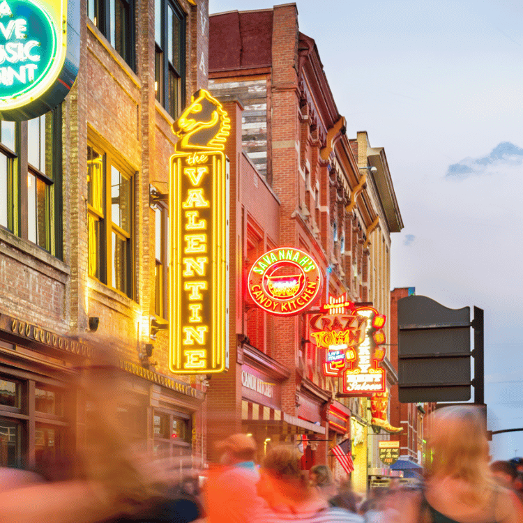 Neon signs on a brick building-lined street, Nashville, blurred figures of people.