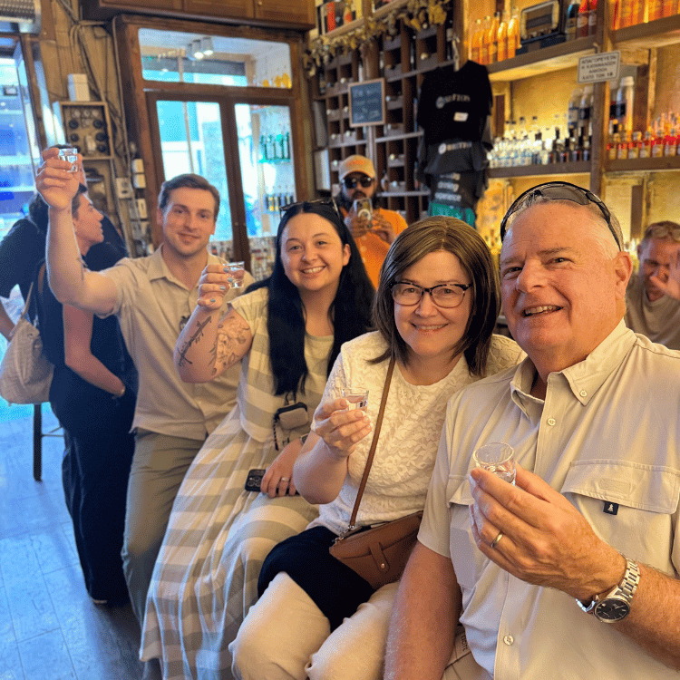 People toasting with small glasses in a bar. Smiling faces, casual attire, bright interior.