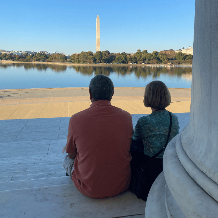 Couple sitting, Washington Monument in distance, reflection in water.