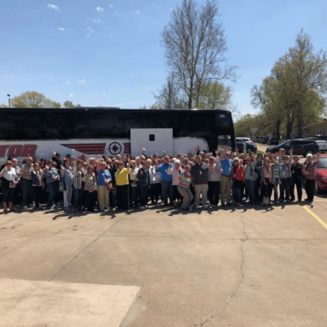 Group of people standing in front of a bus on a sunny day.