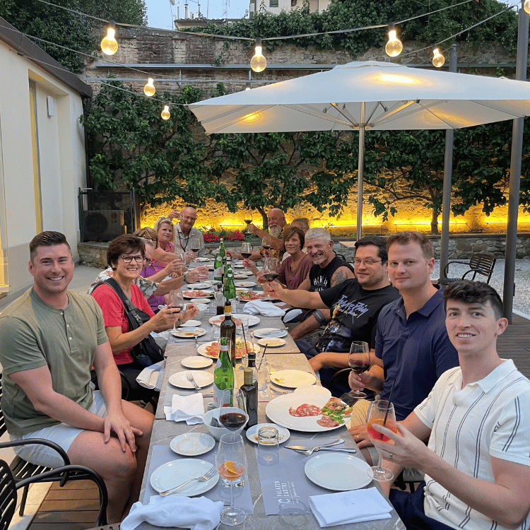 Group of people at an outdoor dinner in Italy, seated around a long table.