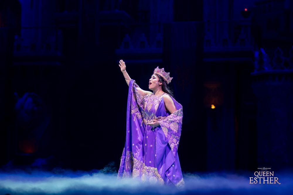 A woman in a purple dress and crown is standing on a stage.
