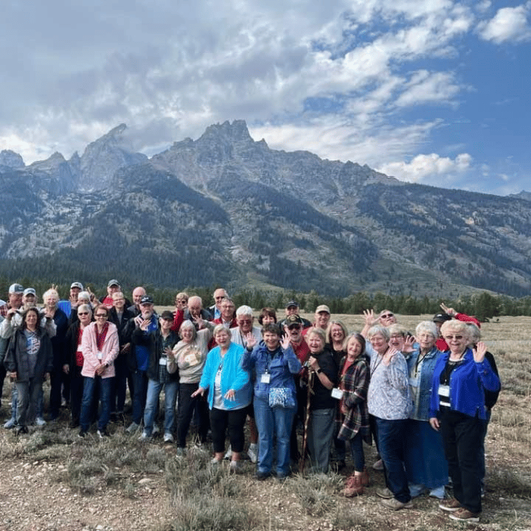 Group of people posing in front of mountains under a cloudy sky.