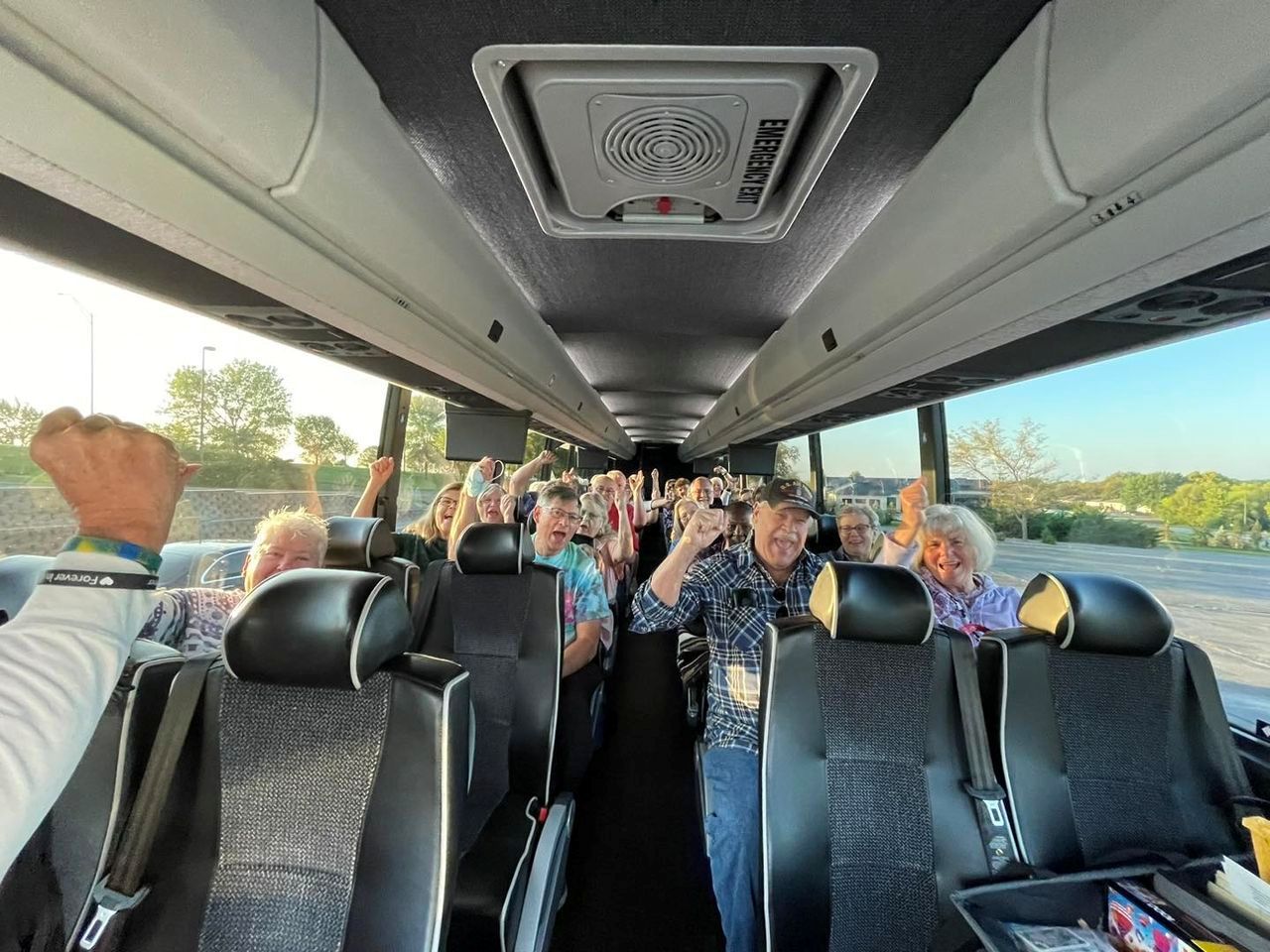 A group of people are sitting on a bus with their hands in the air.