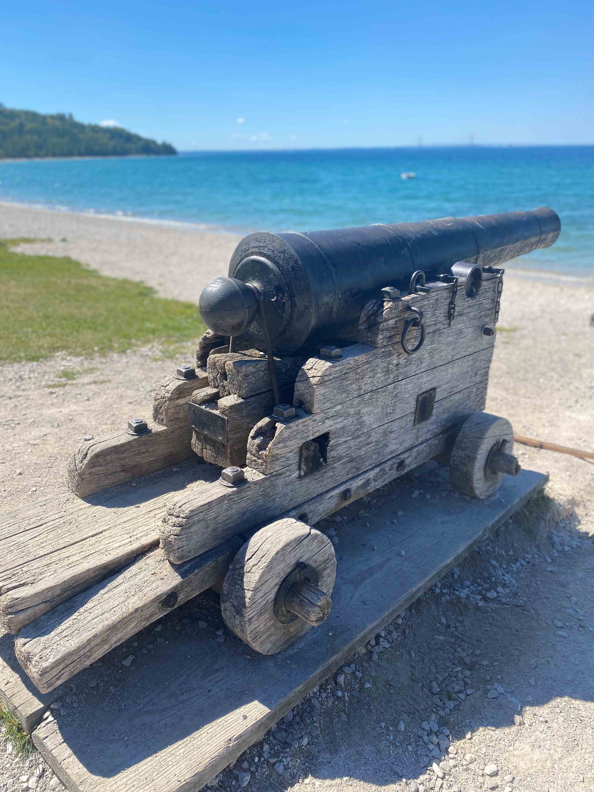 An old cannon on wheels is sitting on a beach next to the ocean.