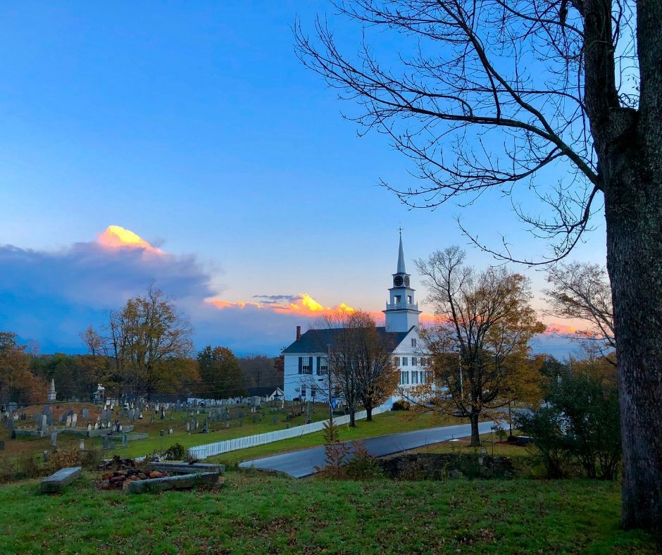 A church is surrounded by trees and a cemetery at sunset