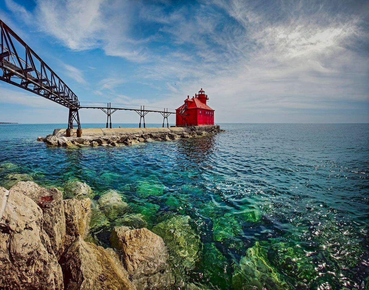 A red lighthouse is sitting on a small island in the middle of the ocean.