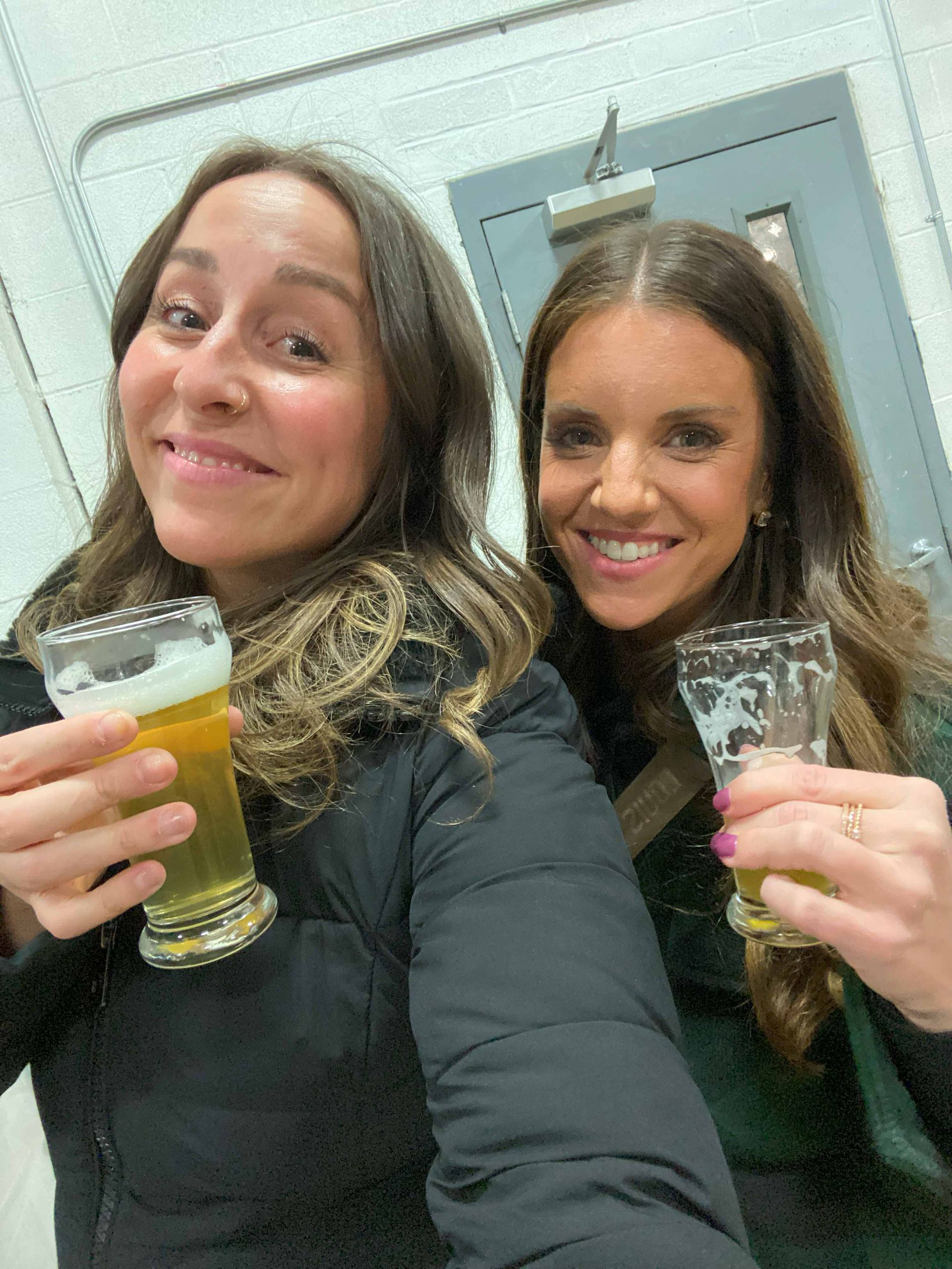 Two women are standing next to each other holding glasses of beer.