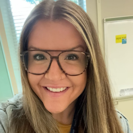 Woman with glasses, smiling. Long hair, looking at the camera. Neutral background.