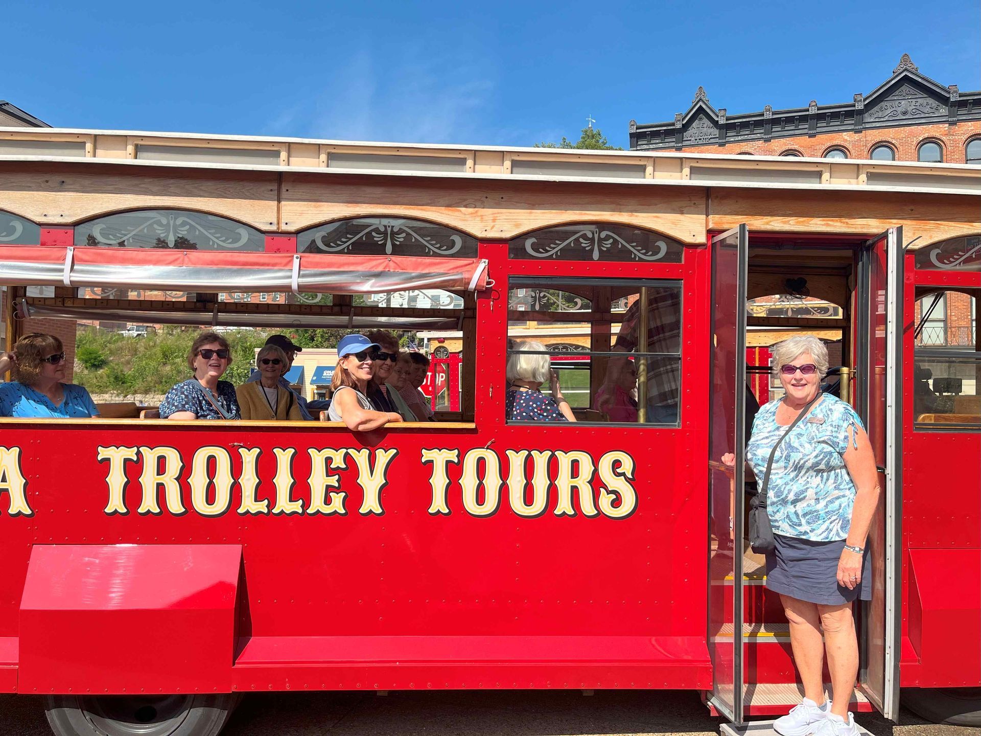 A woman is standing in front of a red trolley tours bus.
