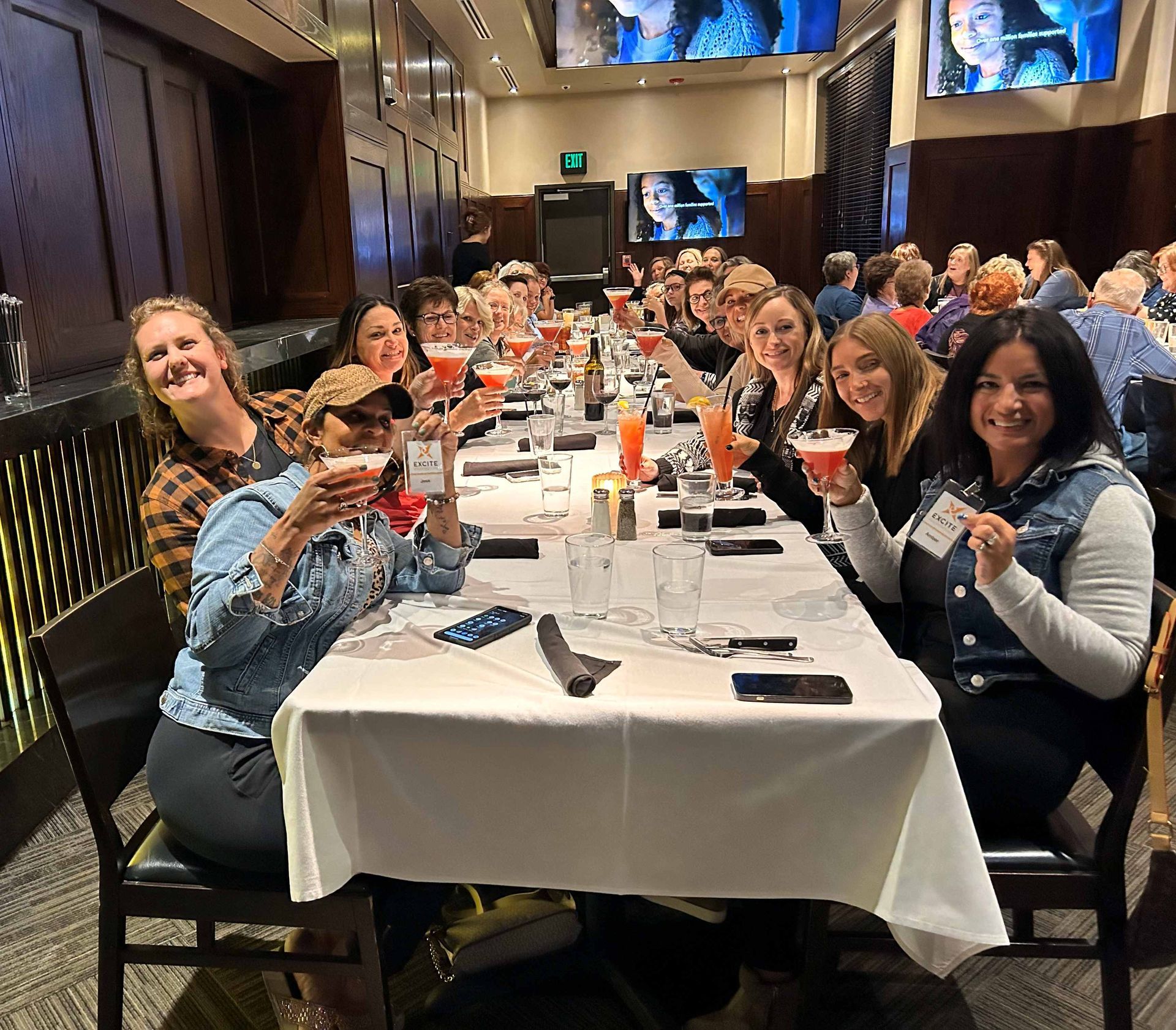 A group of people are sitting at a long table holding drinks.