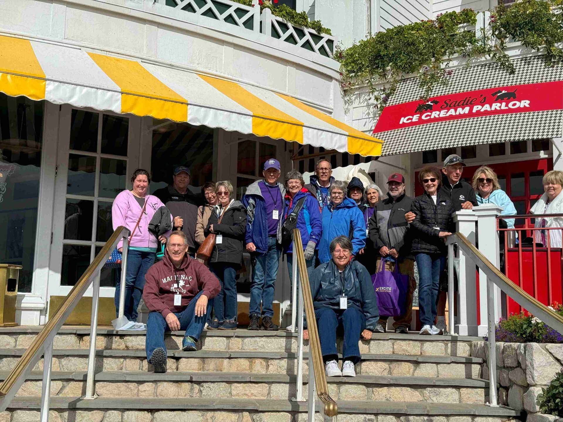 A group of people are posing for a picture on the steps of an ice cream parlor.