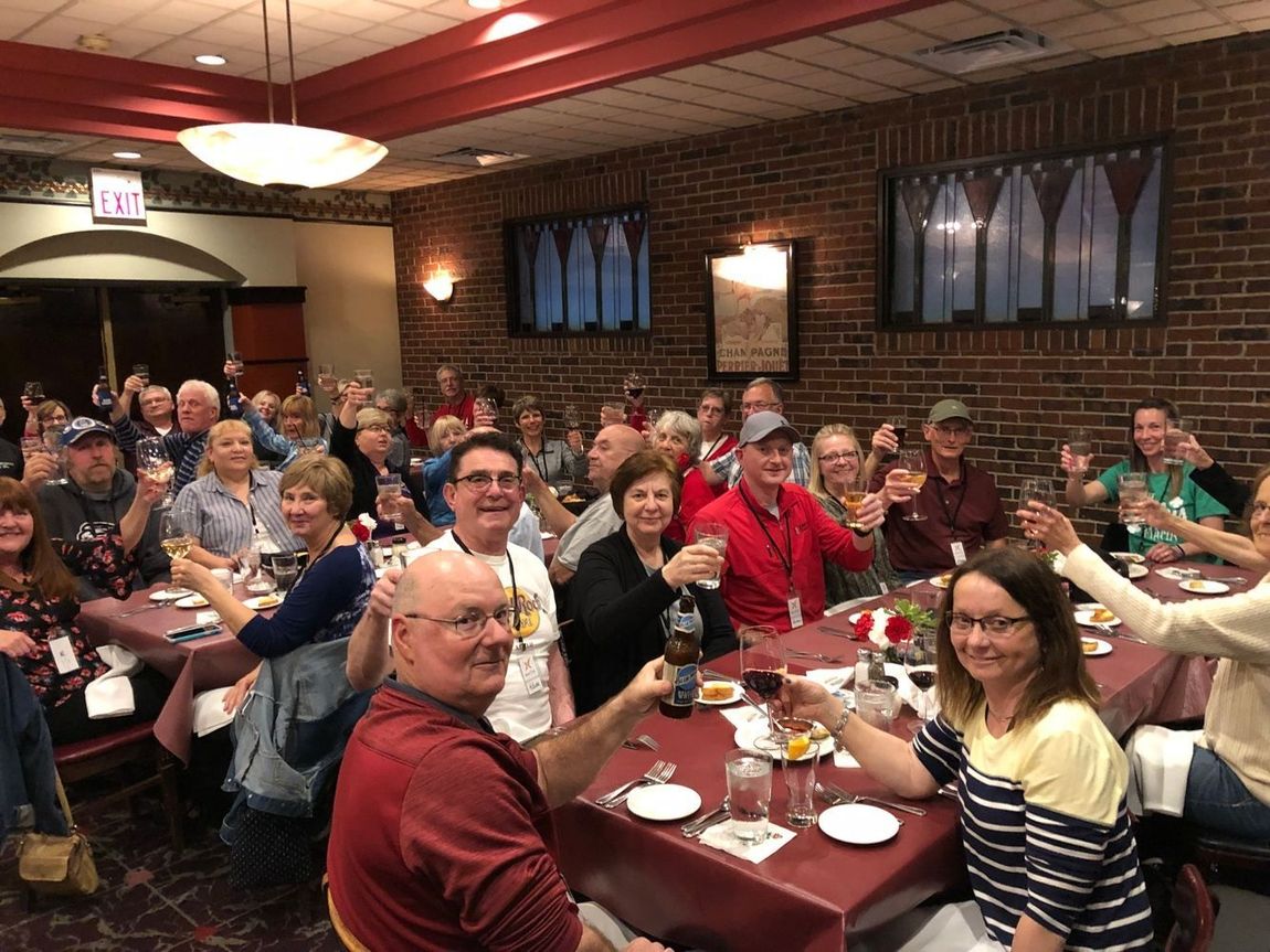 A large group of people are sitting at tables in a restaurant toasting with wine glasses.