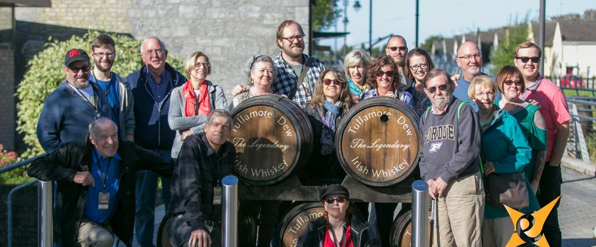 Group of people posing with whiskey barrels outdoors.