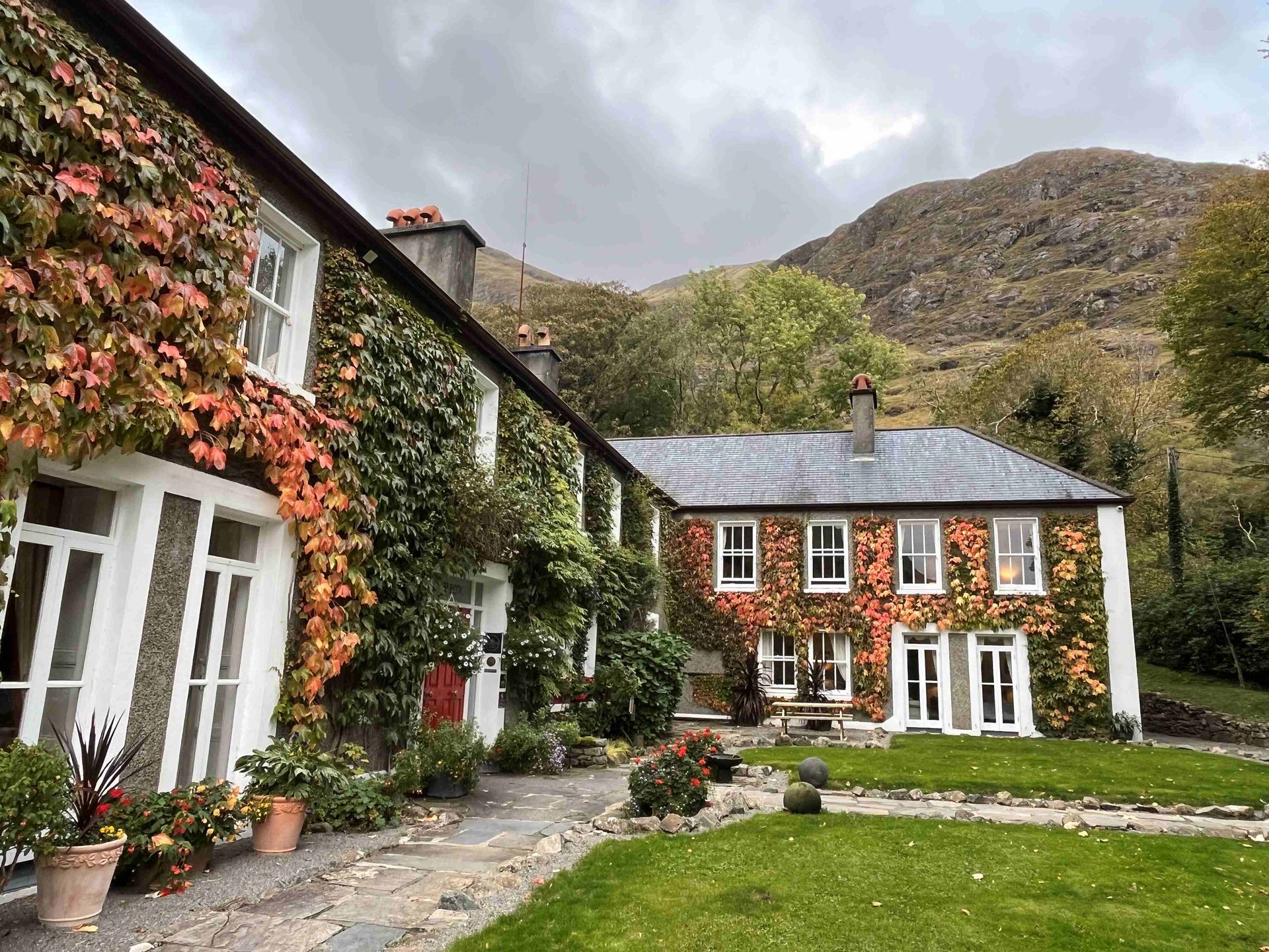 A large house with a lush green lawn in front of it and a mountain in the background.