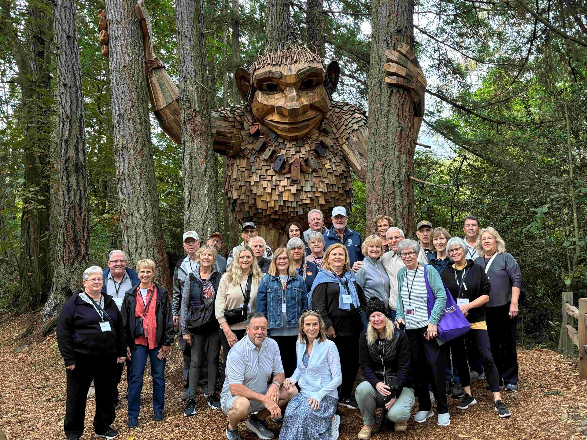 A group of people are posing for a picture in front of a statue in the woods.