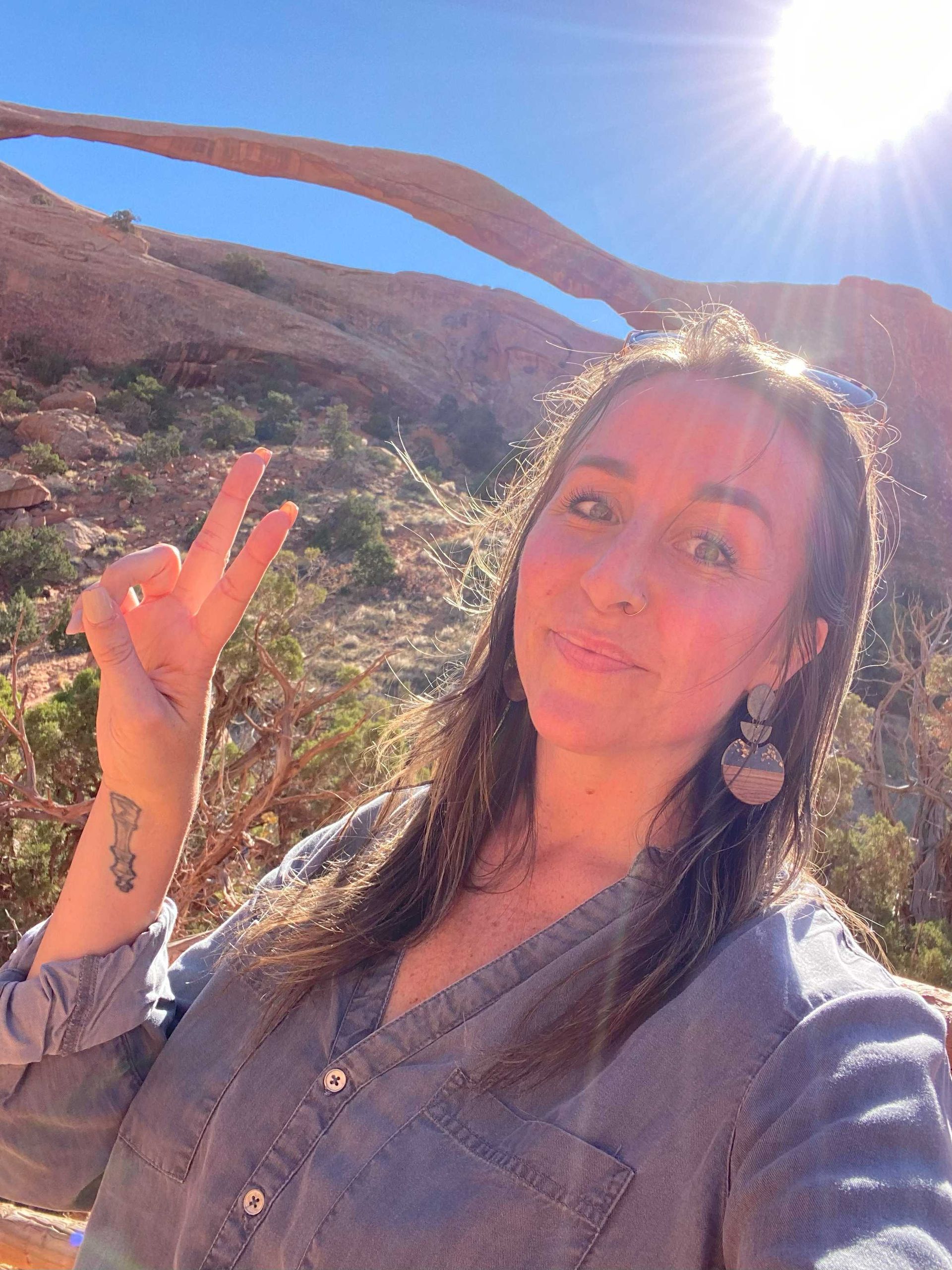 A woman is giving a peace sign in front of a mountain.