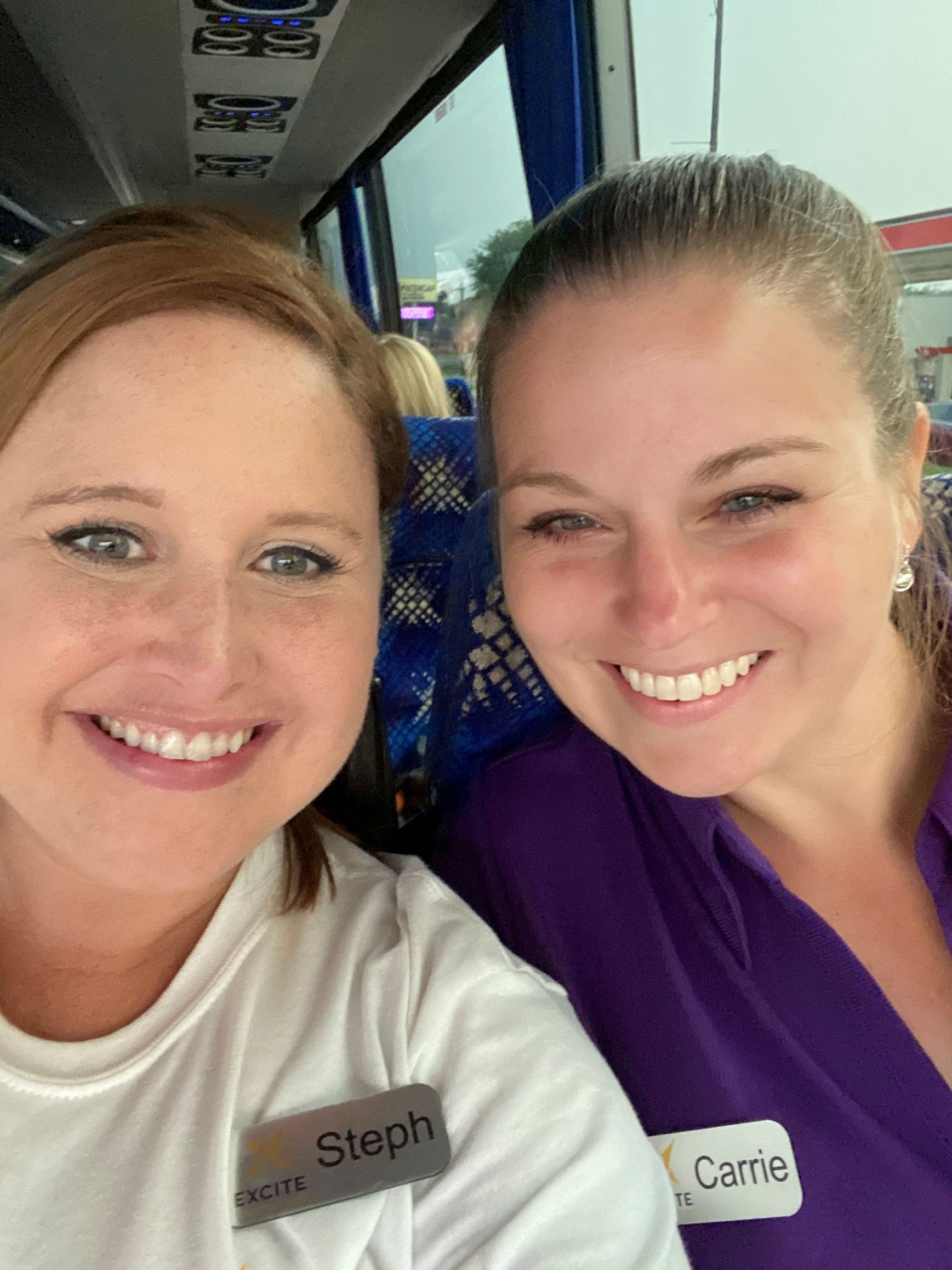 Two women are smiling for a picture while sitting on a bus.